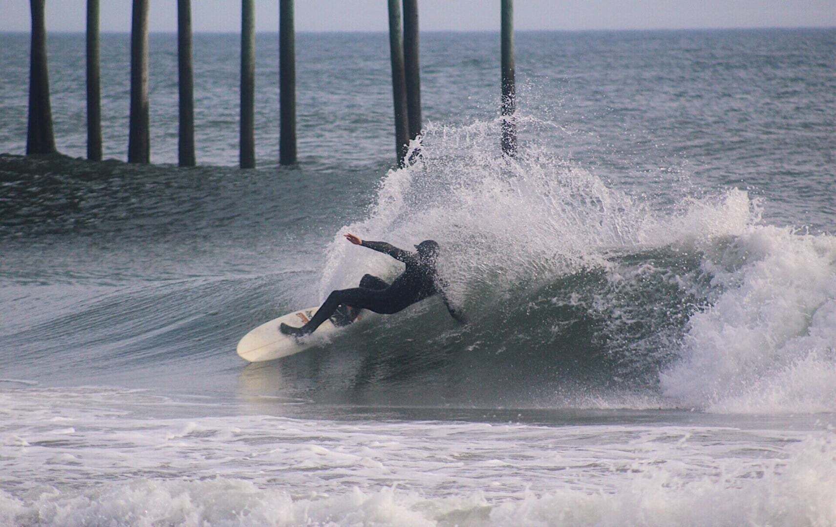 Un surfista cabalgando una ola con un muelle al fondo.
