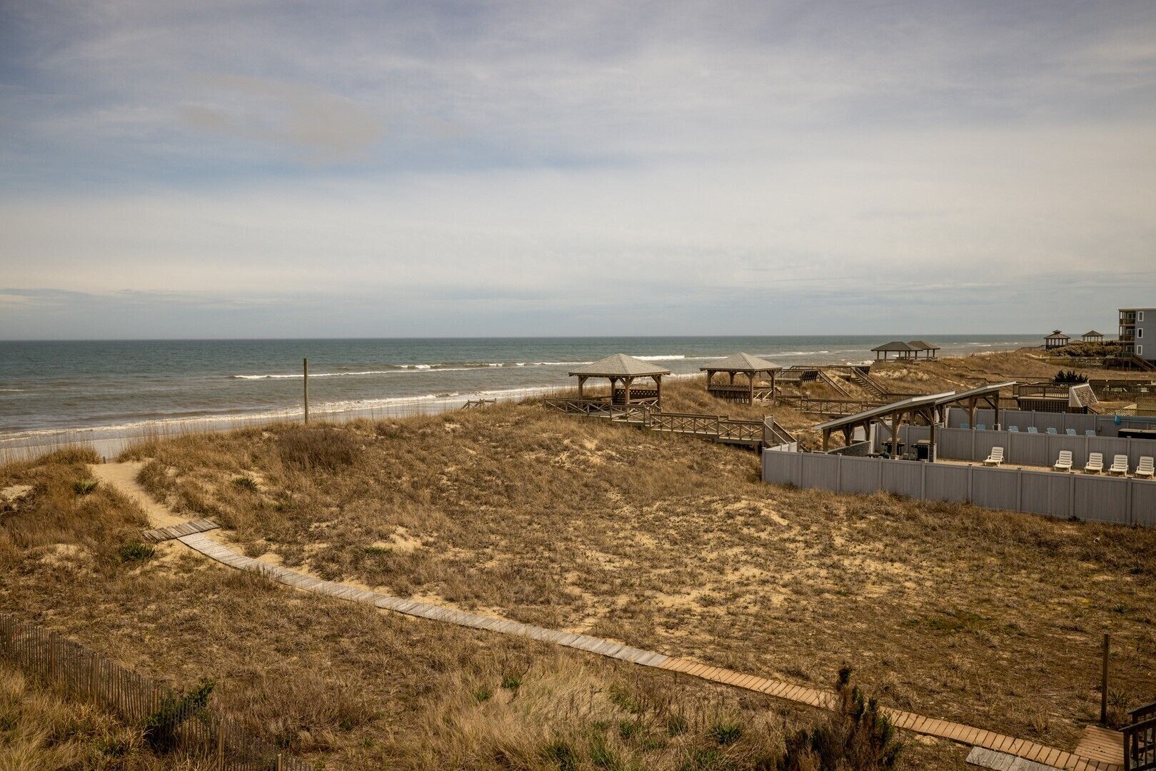 A beach area with wooden walkways, beach huts, and a building with a balcony overlooking the ocean.