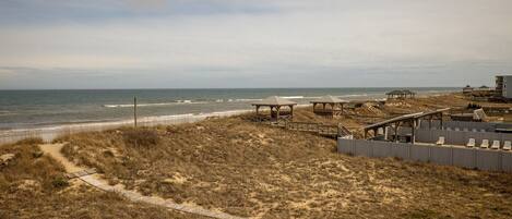 A beach area with wooden walkways, beach huts, and a building with a balcony overlooking the ocean.