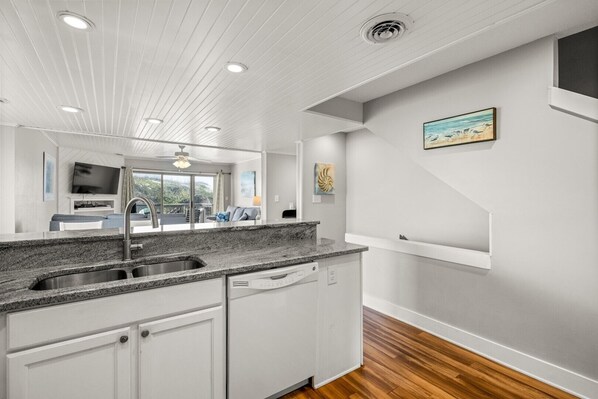 Moderni keittiö, jossa on valkoiset kaapit, graniittitasot ja puulattia.
