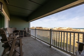 A covered outdoor area with a view of the beach, wooden chairs, a table, and a railing.