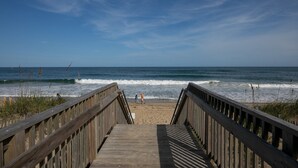 A wooden boardwalk leading to a beach with waves crashing onto the shore. - SC301- Langman's Sea Cabin by First Flight Rentals (Kill Devil Hills)
