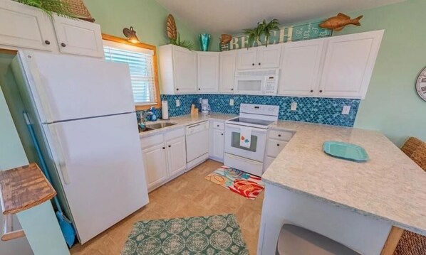 Una cocina compacta con armarios blancos, un refrigerador, un microondas y un lavamanos.