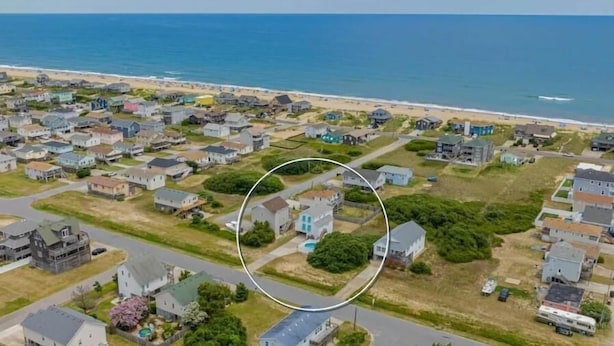 An aerial view of a coastal residential area with houses, a beach, and a clear sky.