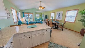 A kitchen with a central island, a dining area with a table and chairs, and a living room with a sofa and a television.