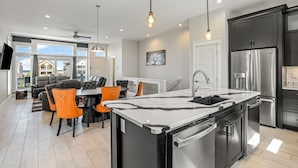 Een moderne keuken met een centraal kookeiland, roestvrijstalen apparatuur en een eethoek met oranje stoelen.