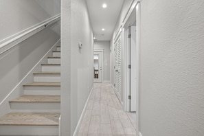 A narrow hallway with a wooden staircase on the left and a door with louvered shutters on the right.