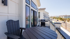 Een balkon met een tafel, stoelen, een barbecue en uitzicht op een woonstraat.