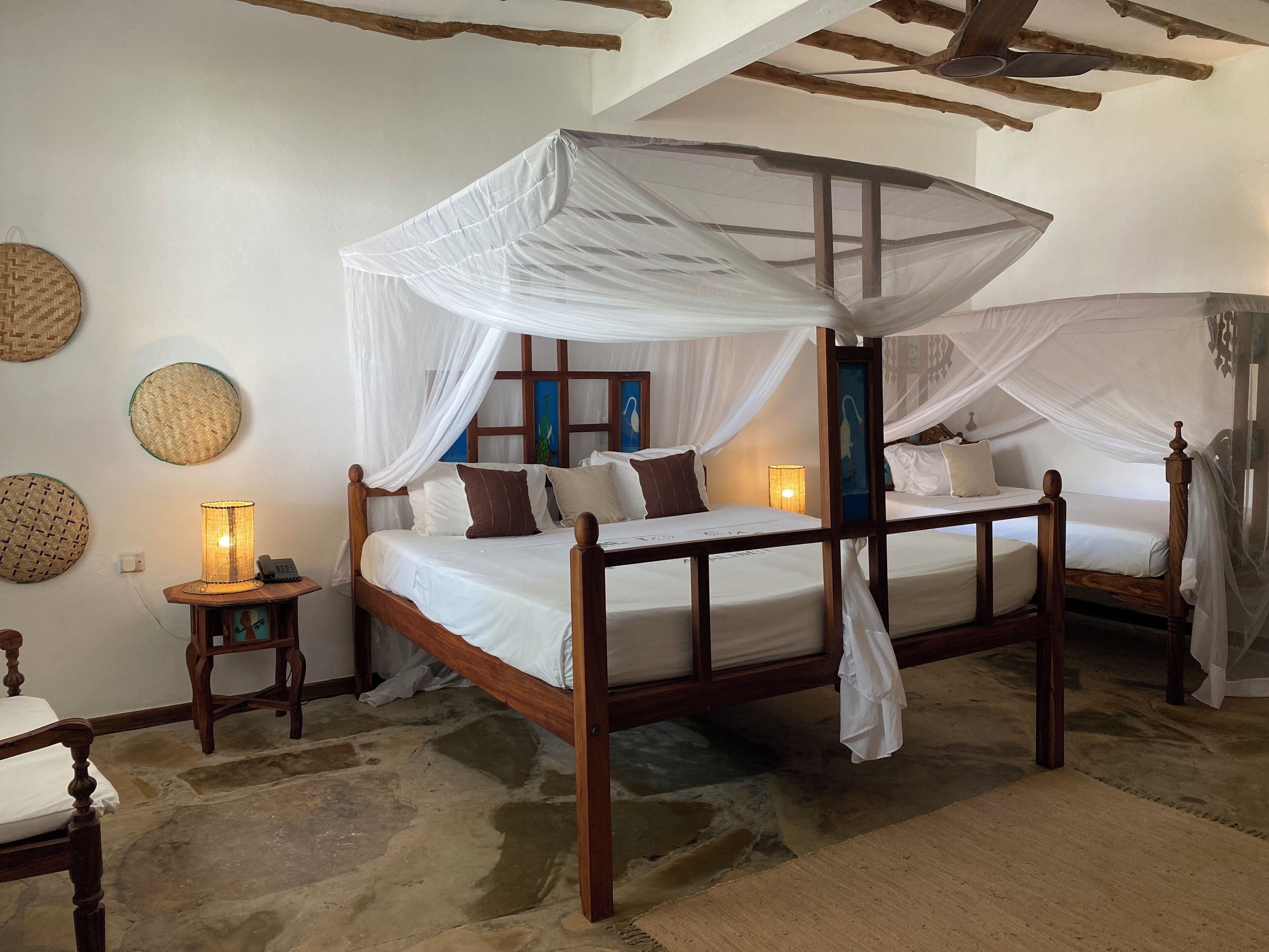 A four-poster bed with white canopy, wooden headboard, and a bedside table with a lamp.