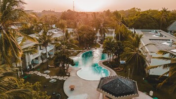 Un resort con piscina central, palmeras y varios edificios con balcones.
