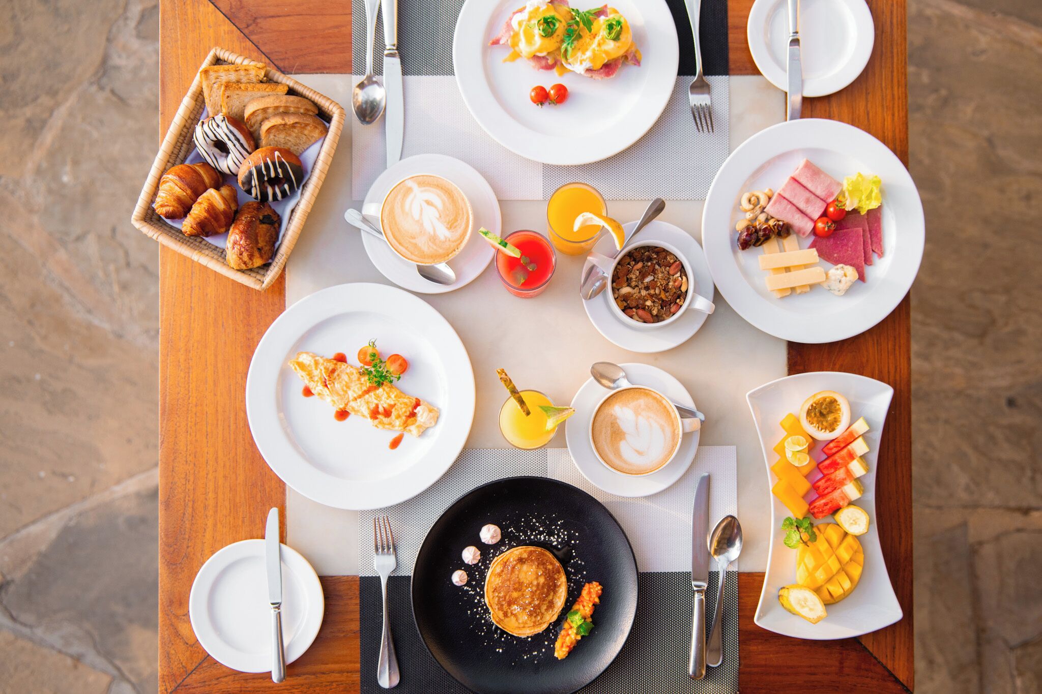 A breakfast setting with various dishes, including croissants, pancakes, and a fruit platter.