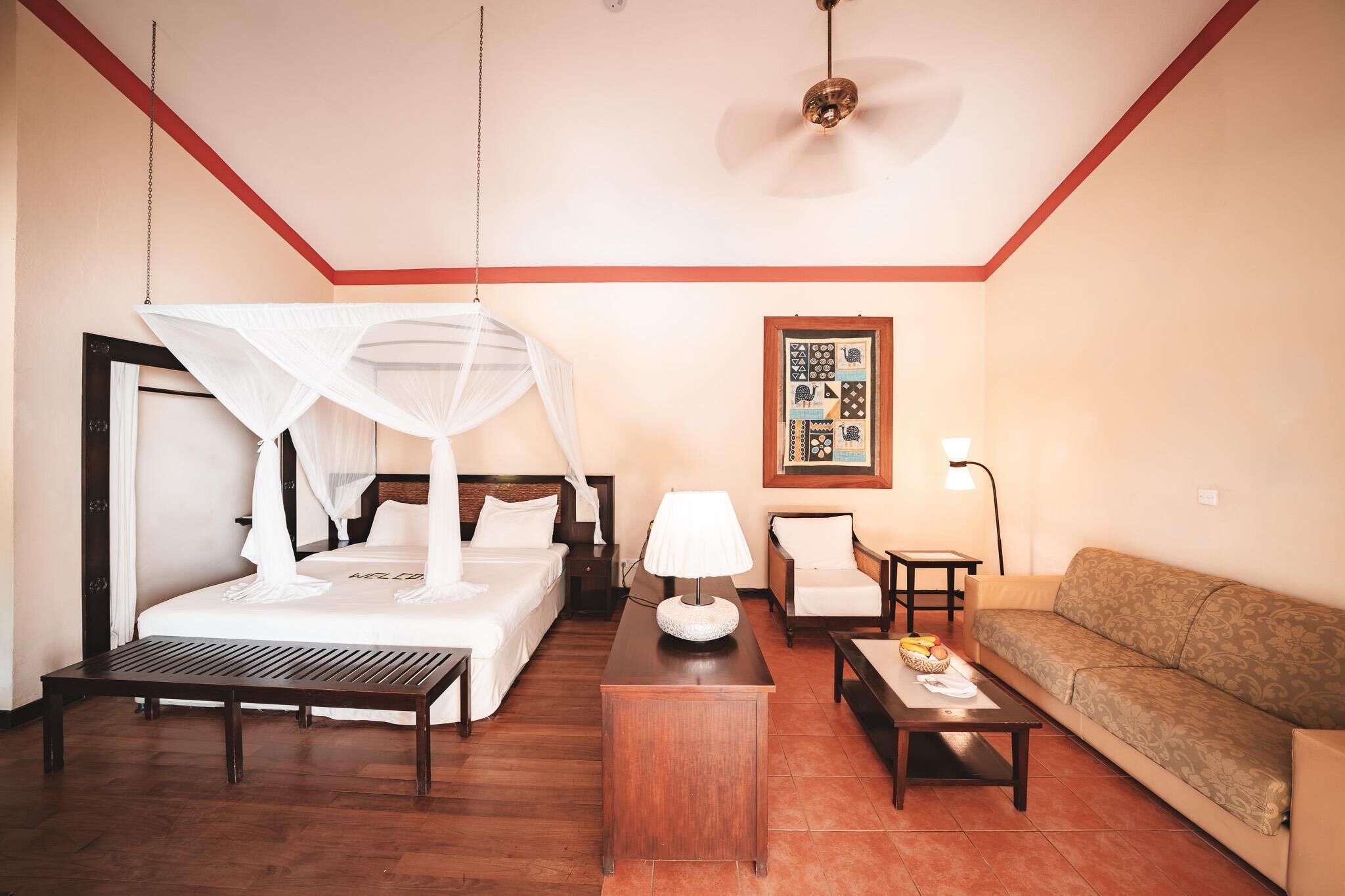 A hotel room with a bed, a sofa, a small table, a lamp, and a ceiling fan.