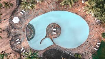 Vista aérea de una piscina con un diseño espiral único, rodeada de baldosas de piedra y palmeras.