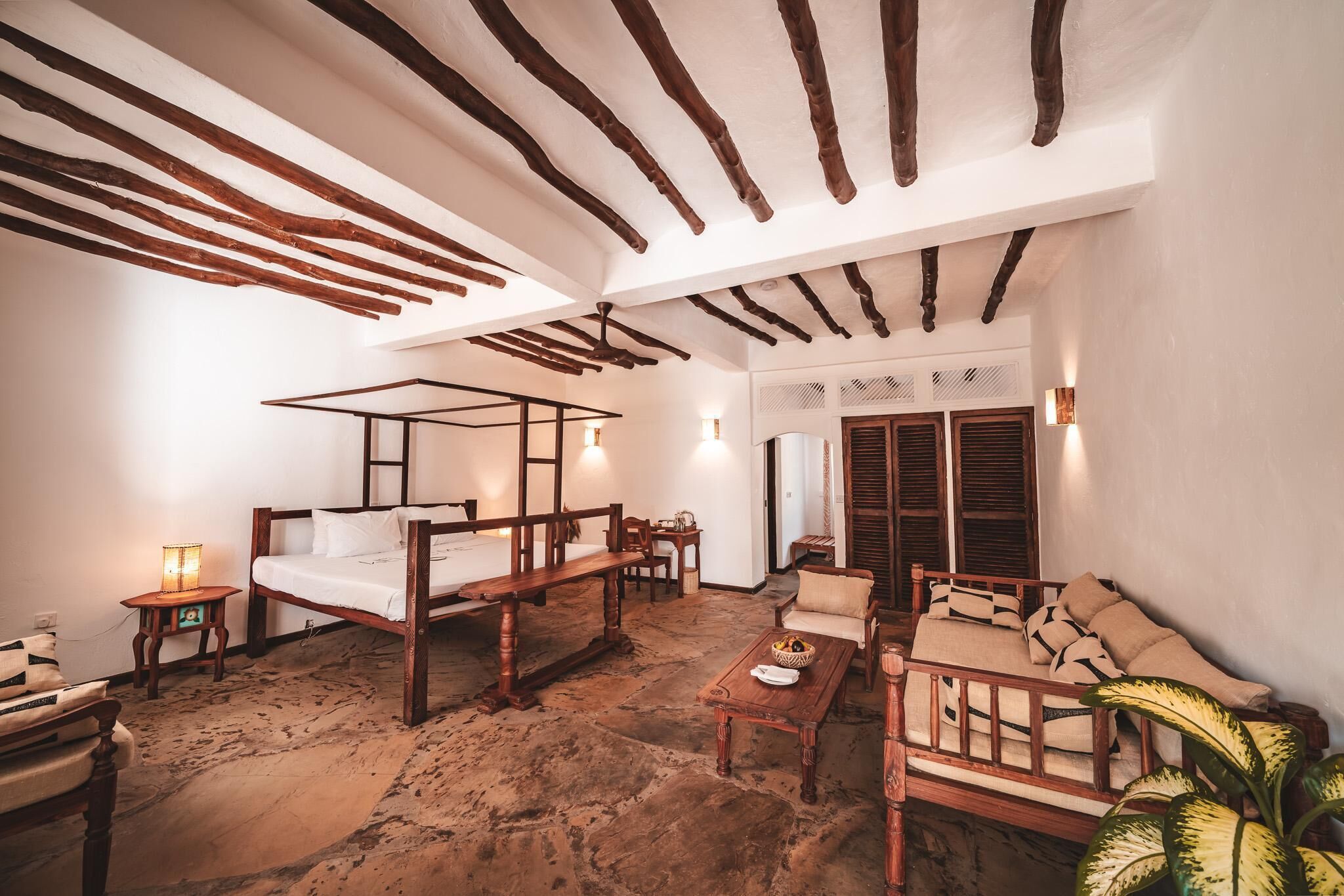 A room with a four-poster bed, a sofa, a wooden coffee table, and a small table with a lamp.