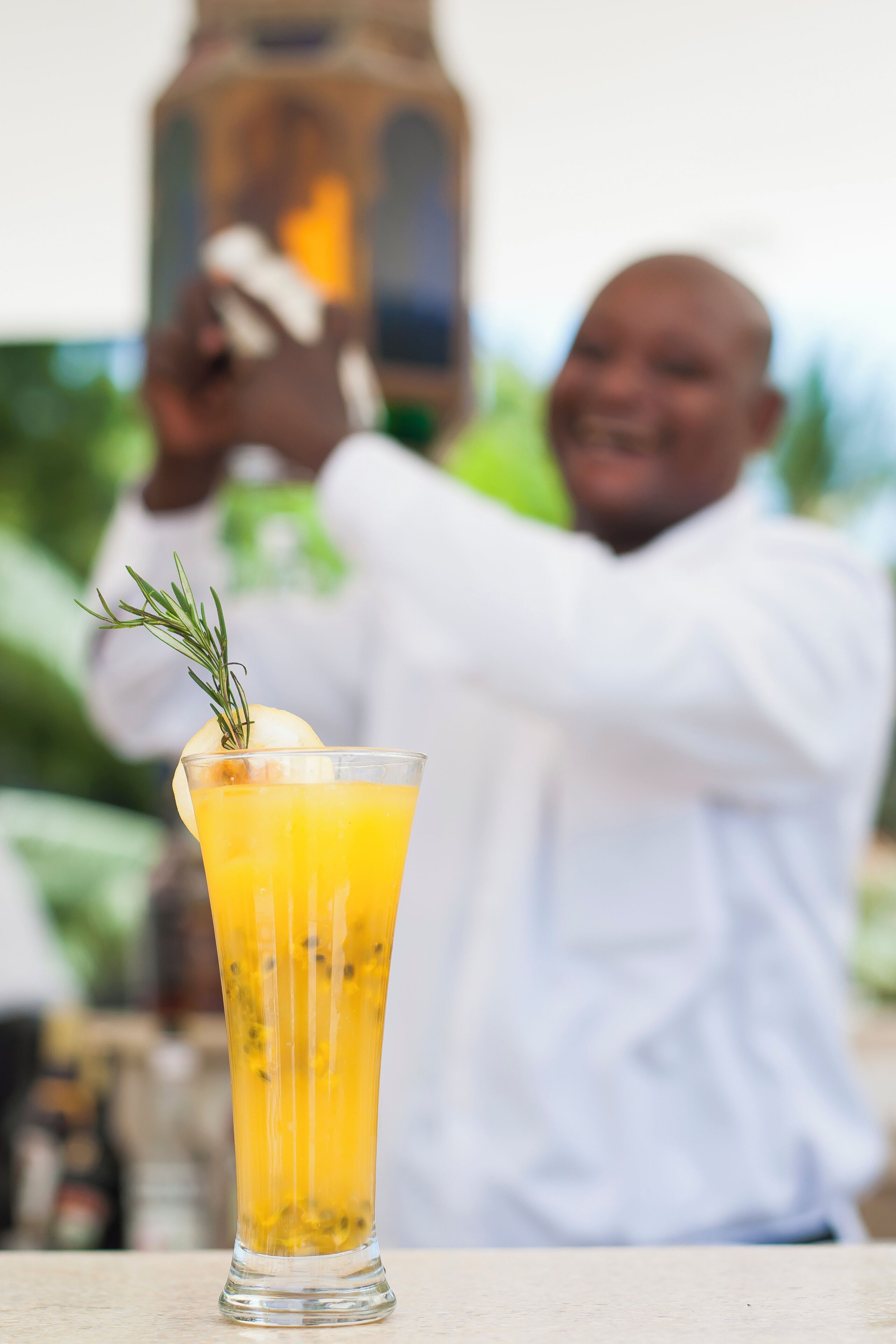 A tall glass of orange juice with a sprig of rosemary, placed on a table.