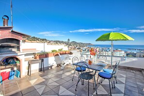 A patio with a table and chairs, a green umbrella, and a view of the sea.