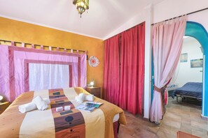 A hotel room with a bed, a nightstand, a lamp, and a view through an archway.