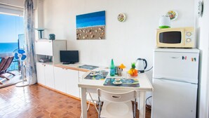 A kitchen with a dining table, chairs, a microwave, a refrigerator, and a beach-themed painting. - Sole Surf E Relax, Sea-view Balcony Apartment (Sanremo)