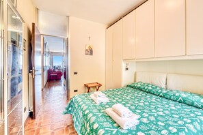 Quarto de hotel com cama, uma mesa pequena, uma cadeira e vista através de uma porta aberta.