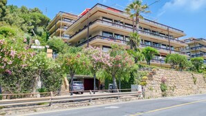 A multi-story hotel with balconies, a stone retaining wall, and a parking area. - Casa 3 Ponti With Sea-view Balcony and Parking (Sanremo)