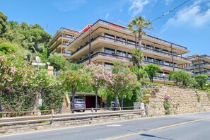 Um hotel de vários andares com varandas, um muro de pedra de suporte e uma área de estacionamento.