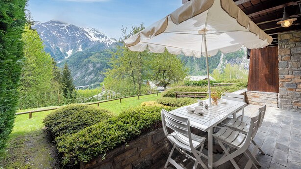 A patio with a table and chairs, a white umbrella, and a mountain view. - Plan Gorret Wonderful Apartment In Courmayeur (Courmayeur)