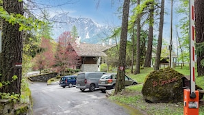 A parking area with vehicles, a stone wall, and a building with a tiled roof. - Plan Gorret Wonderful Apartment In Courmayeur (Courmayeur)