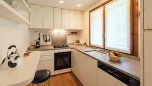 A modern kitchen with white cabinets, a built-in oven, a dishwasher, and a window with a view. - Plan Gorret Wonderful Apartment In Courmayeur (Courmayeur)