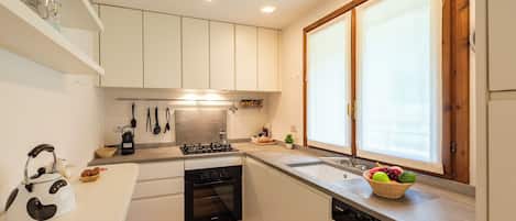 Cocina moderna con armarios blancos, horno empotrado, lavavajillas y ventana con vistas.