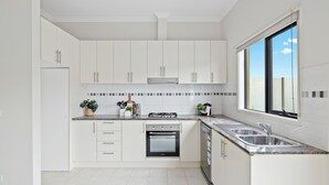 Cozinha moderna com armários brancos, forno embutido, pia de aço inoxidável e janela com vista para o céu.