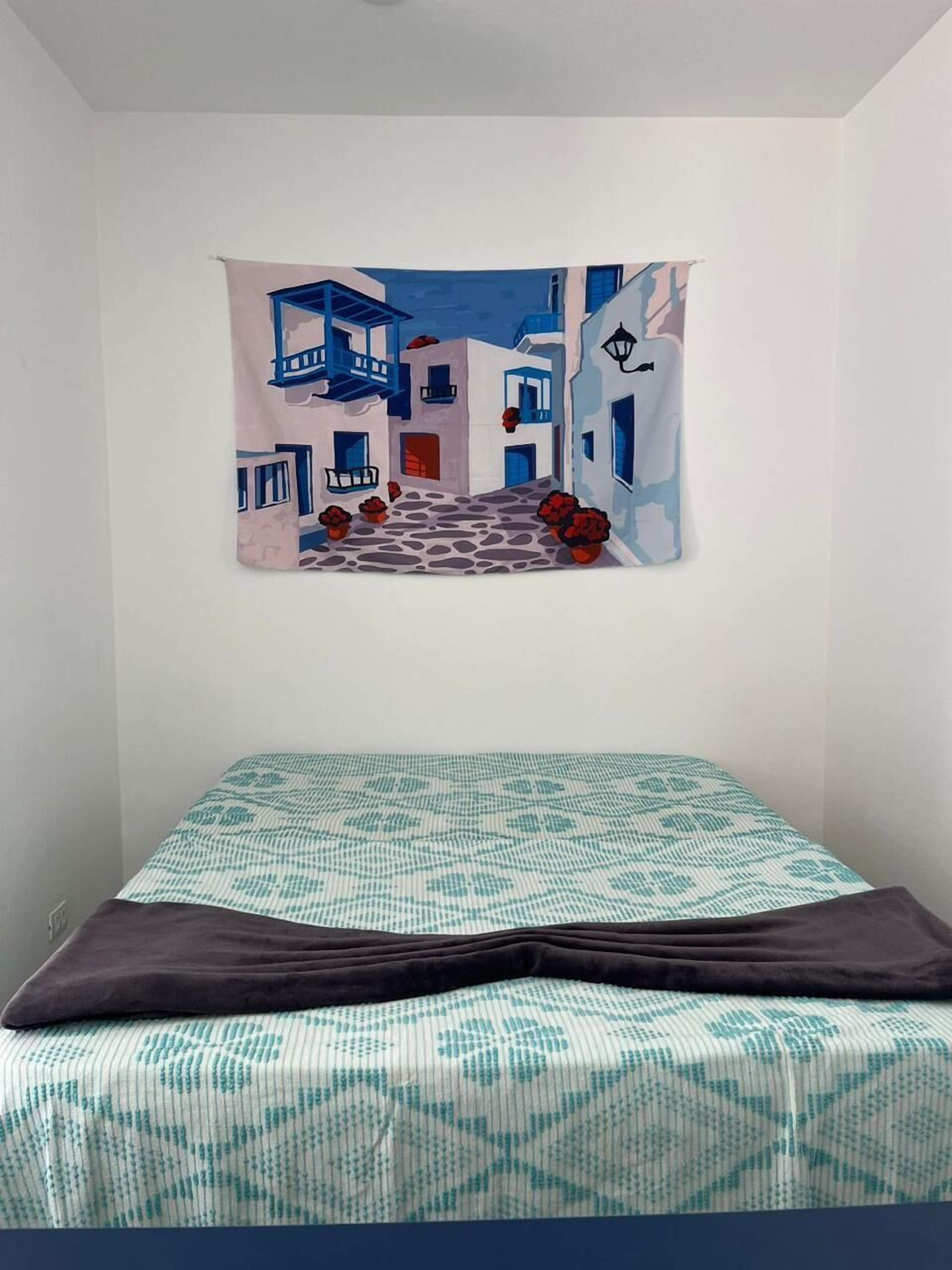 A bedroom with a bed, a wall tapestry, and a patterned bedspread.