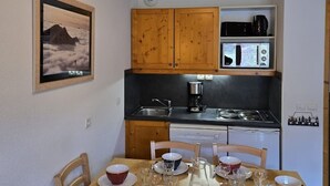 A compact kitchen with wooden cabinets, a stove, and a dining table set for four.