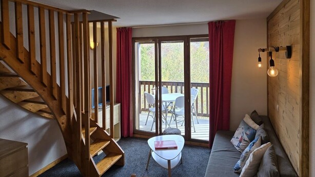 A room with a wooden staircase, a sofa, a small table, and a balcony with a view.