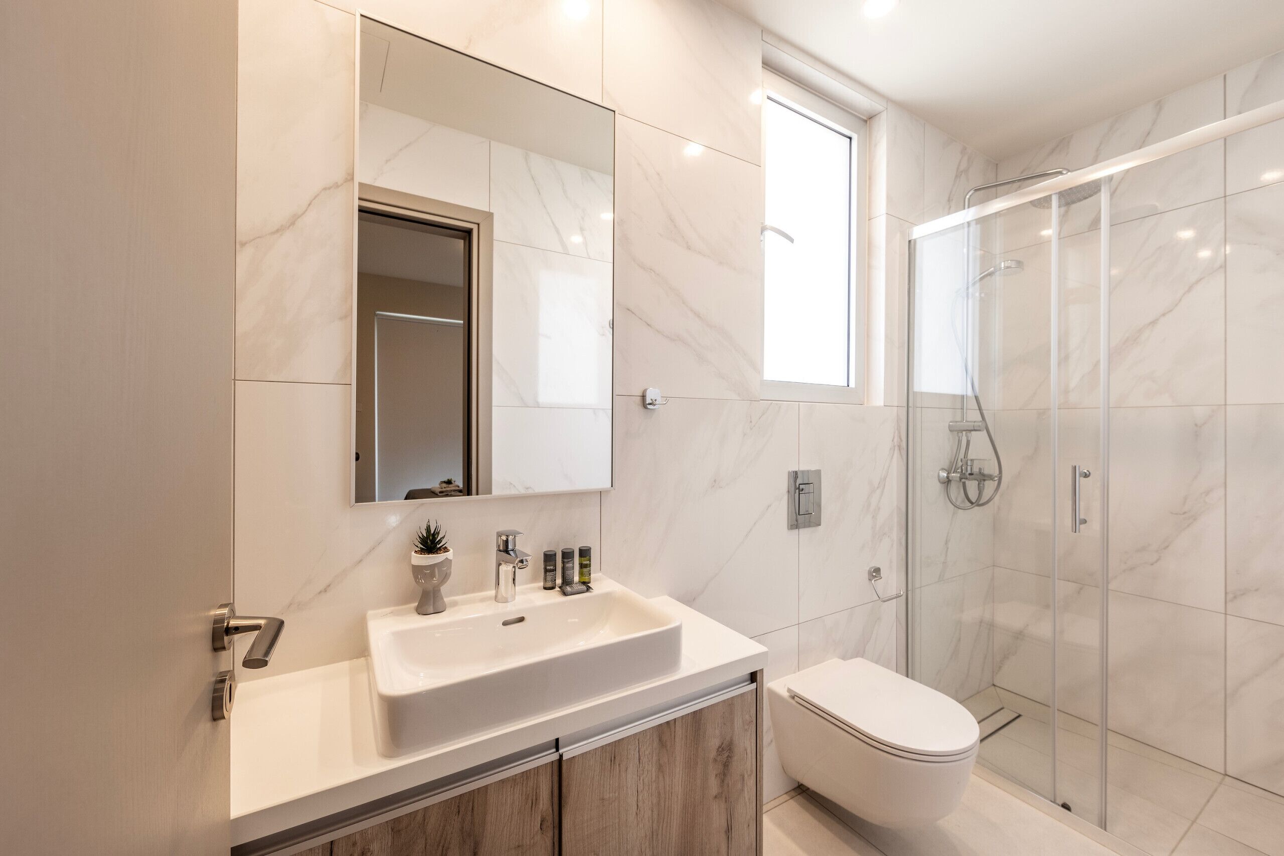 A modern bathroom with a marble sink, a toilet, and a glass-enclosed shower.