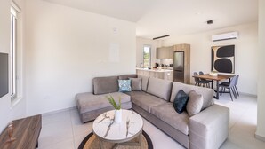 A modern living room with a sectional sofa, a coffee table, and a dining area with a table and chairs. - Protaras Mythical Seas (Paralimni)