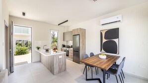 A modern kitchen with a central island, a dining area with a wooden table and chairs, and a large black abstract painting on the wall. - Protaras Mythical Seas (Paralimni)