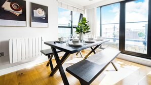 A dining area with a table set for four, a bench, a potted plant, and framed artwork on the wall. - Modern 2BR in Surrey | Pet-Friendly, WiFi, Parking (Surrey)
