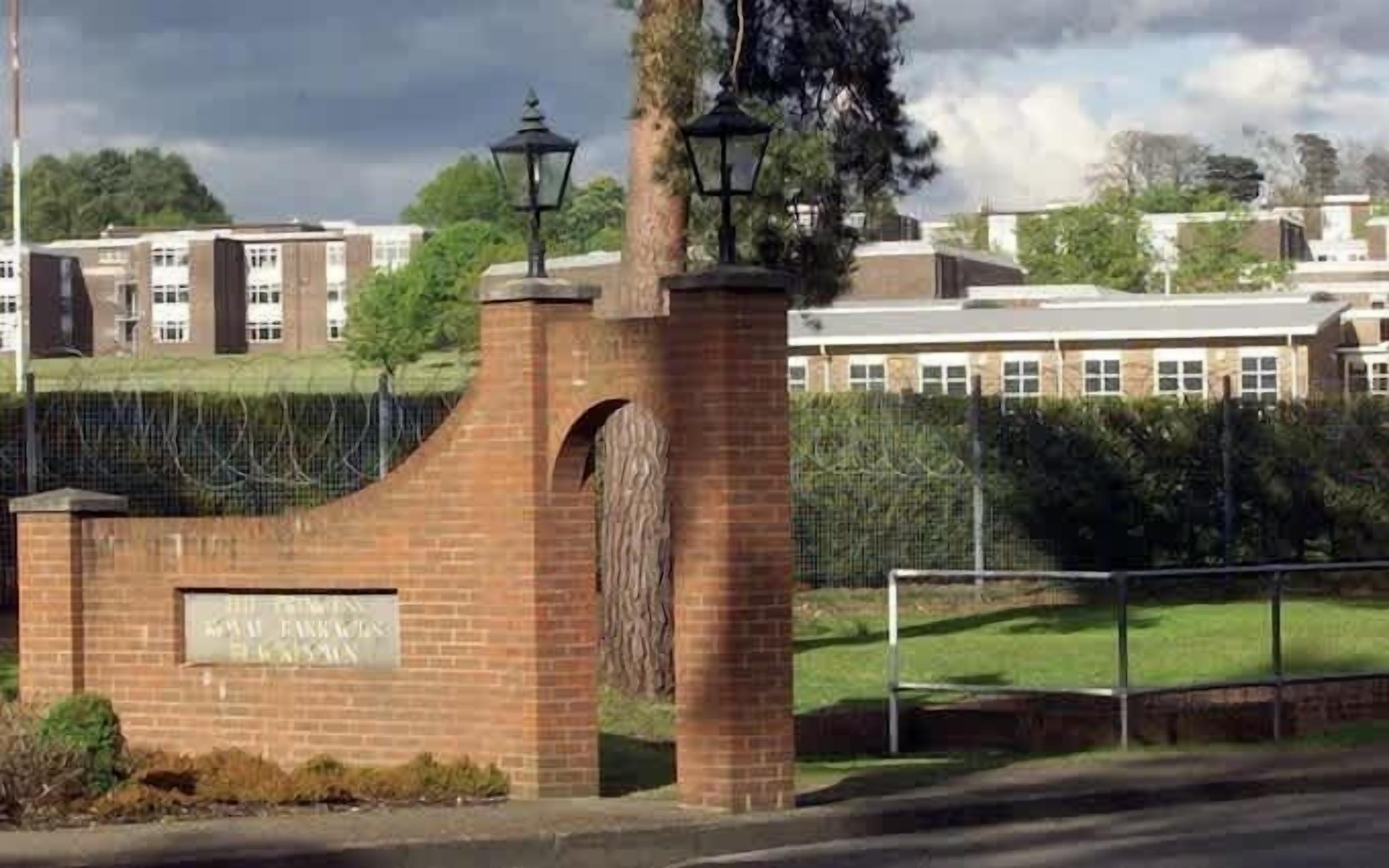 A brick entrance with a sign, a lamp post, and a fence.