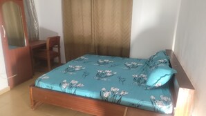 A bedroom with a bed, a wooden chair, a wardrobe, and a curtain. - Assembly Hotel - Esiama  (Esiama)
