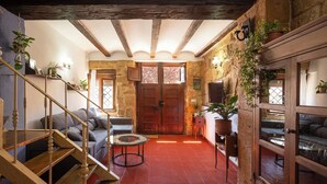 A rustic interior with a wooden staircase, a sofa, a round coffee table, and a large wooden door.