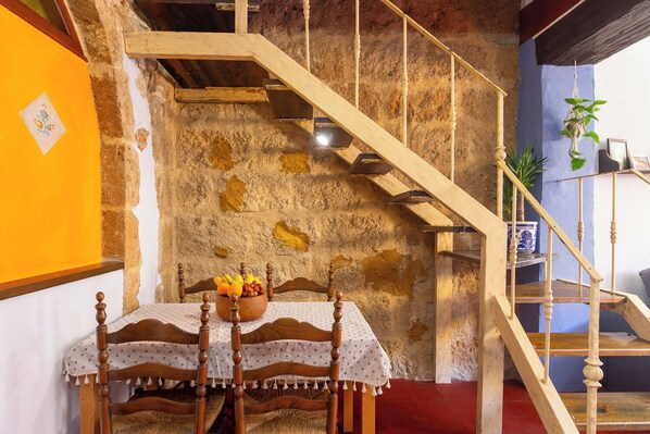 Une pièce rustique avec un escalier en bois, une table à manger sur laquelle se trouve un panier de fruits et une plante en pot.