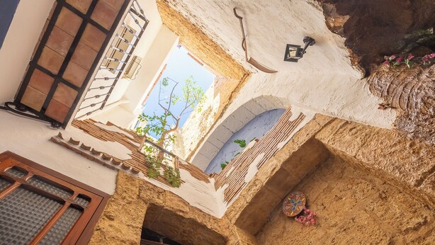 A courtyard with a wooden door, a window with a grid pattern, and a wall with a decorative tile.