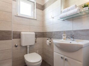 A modern bathroom with a toilet, sink, and glass shelf with towels. - Attila A2 Apartments, Ciovo Island (Okrug Gornji)