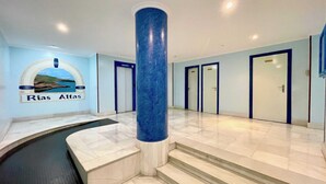 Un hall d’hôtel avec un sol en marbre, une grande colonne bleue et une enseigne indiquant « Rias Altas ».