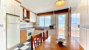 Une cuisine équipée d’une table à manger, de chaises, d’un four à micro-ondes et offrant une vue sur la mer par les fenêtres.