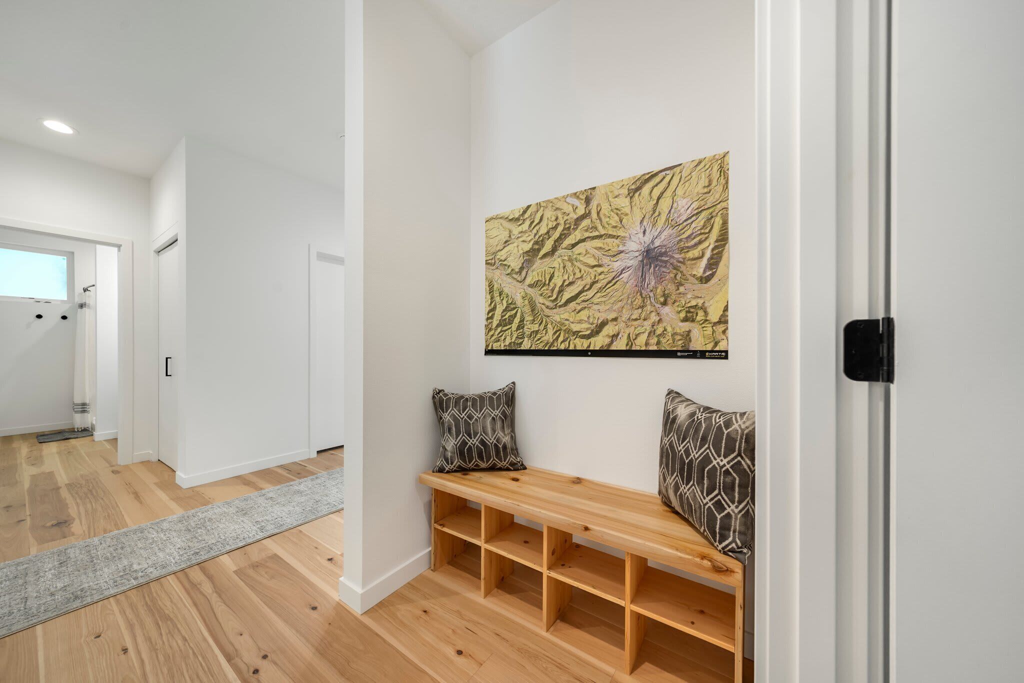 A hallway with a wooden bench, two patterned pillows, and a large abstract painting on the wall.
