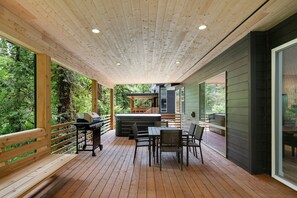A wooden deck with a grill, dining table, and chairs, overlooking a forested area. - Sandy River Group Getaway 4 (Mount Hood Village)