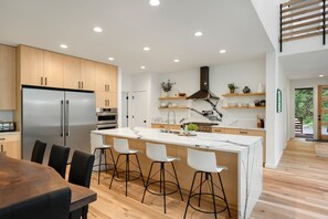 A modern kitchen with a central island, bar stools, a refrigerator, oven, and a stove. - Sandy River Group Getaway 4 (Mount Hood Village)