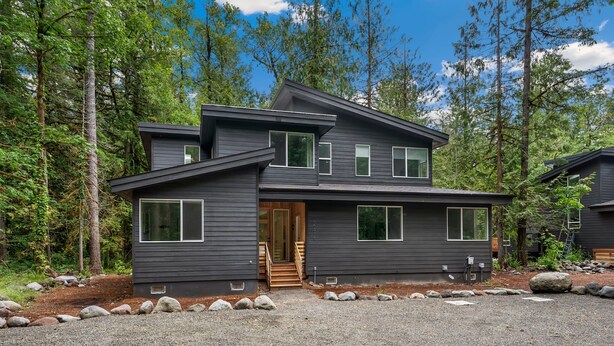 A two-story modern house with a stone foundation, large windows, and a wooden front door. - Sandy River Group Getaway 4 (Mount Hood Village)