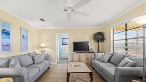 A living room with two grey sofas, a coffee table, a ceiling fan, a TV, and a window with blinds. - Awesome & Affordable 3 Bdrm, 2 Ba with easy beach access, and Gulf & Bay Views.  (Gulf Shores)